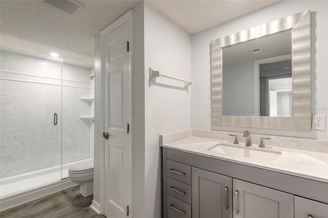 bathroom with a textured ceiling, wood finished floors, toilet, vanity, and a shower stall
