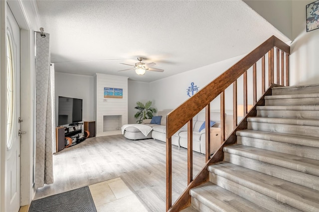 staircase featuring ceiling fan, a fireplace, and a textured ceiling