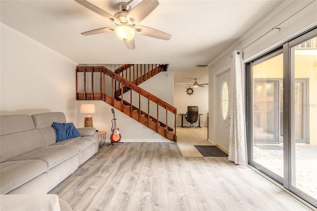 unfurnished living room with ceiling fan, light wood-type flooring, crown molding, stairs, and a textured ceiling