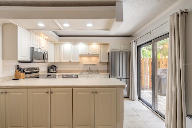 kitchen featuring appliances with stainless steel finishes, a sink, a peninsula, light countertops, and ornamental molding