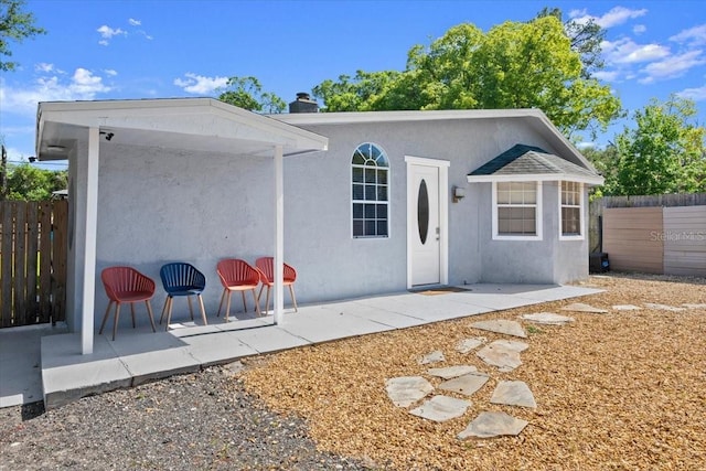 rear view of property with stucco siding, a patio area, fence, and a chimney