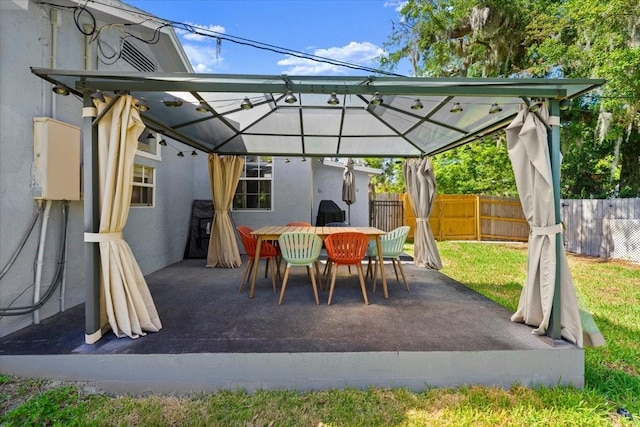 view of patio with a gazebo, outdoor dining space, and fence