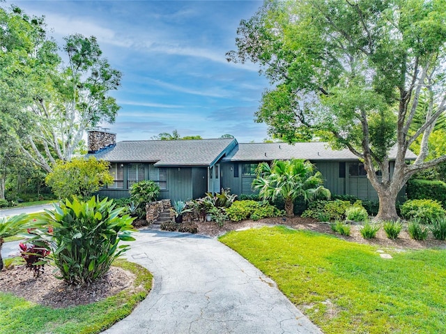 single story home featuring roof with shingles, driveway, a chimney, and a front yard