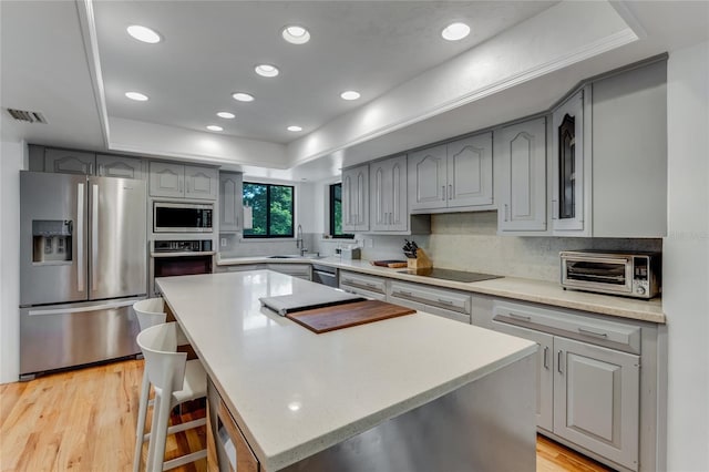 kitchen featuring a sink, a tray ceiling, gray cabinets, visible vents, and appliances with stainless steel finishes