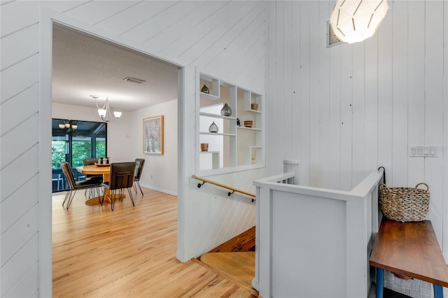 hall featuring a chandelier, wood walls, light wood-type flooring, and an upstairs landing