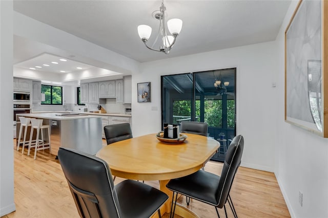 dining area featuring a raised ceiling, a notable chandelier, light wood-type flooring, and baseboards