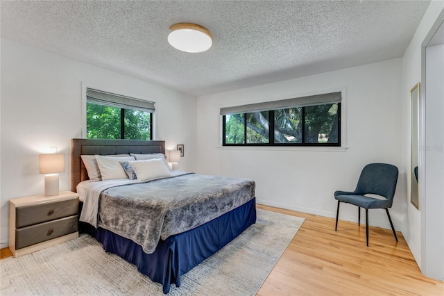 bedroom with light wood finished floors, a textured ceiling, and baseboards
