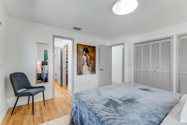 bedroom with baseboards, light wood-style floors, visible vents, and a textured ceiling
