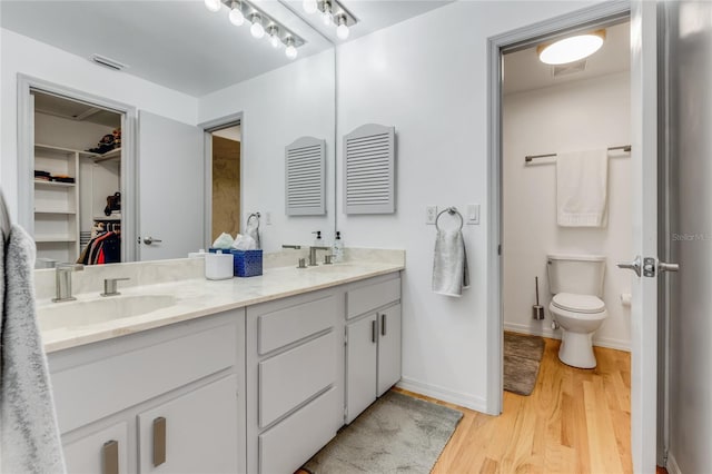 bathroom with a sink, toilet, a walk in closet, wood finished floors, and double vanity
