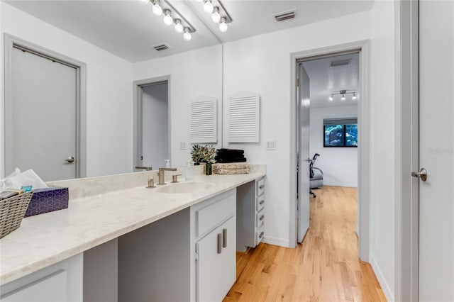 bathroom featuring wood finished floors, vanity, rail lighting, visible vents, and baseboards