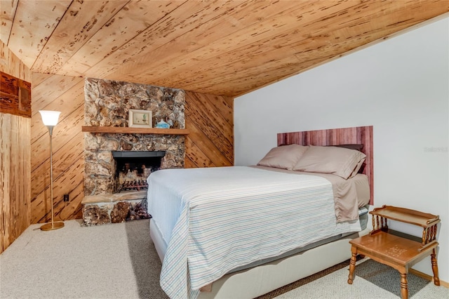 bedroom with wooden walls, wood ceiling, carpet floors, and a stone fireplace