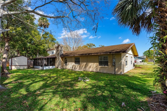 back of house featuring an outbuilding, a storage unit, a sunroom, a lawn, and brick siding