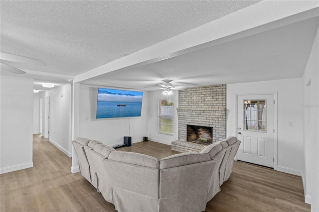 living area featuring a textured ceiling, a brick fireplace, a ceiling fan, and wood finished floors