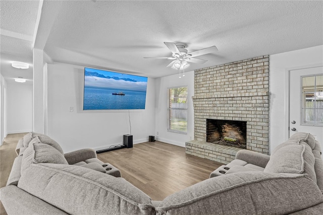 living room featuring a textured ceiling, wood finished floors, a ceiling fan, and a brick fireplace