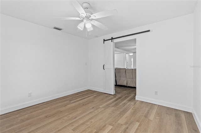 unfurnished room featuring a barn door, visible vents, ceiling fan, baseboards, and light wood-style floors