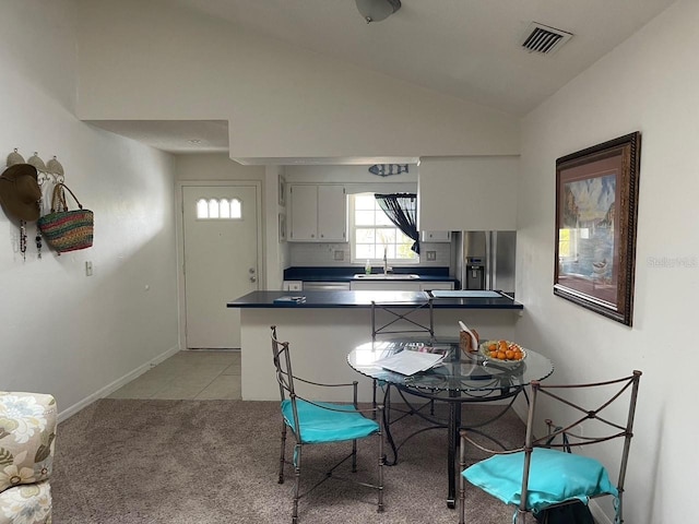 kitchen with dark countertops, stainless steel refrigerator with ice dispenser, white cabinets, visible vents, and vaulted ceiling