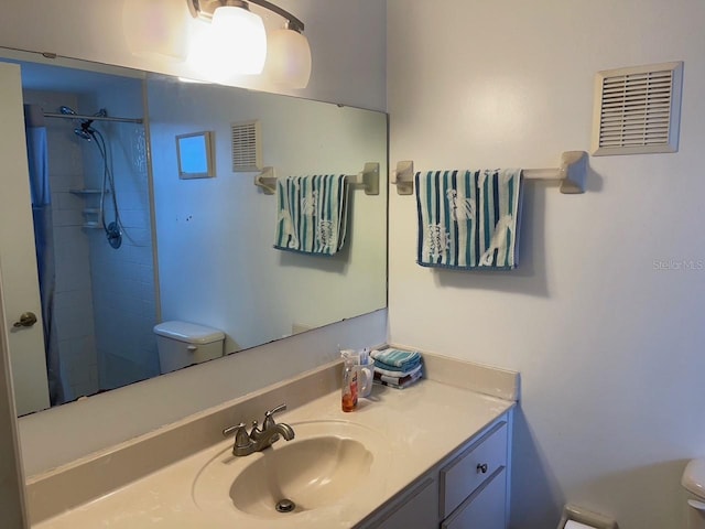 full bathroom featuring toilet, tiled shower, vanity, and visible vents
