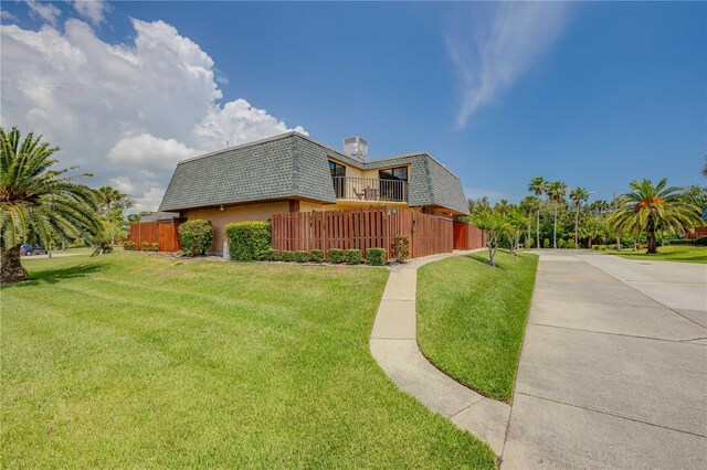 view of property exterior with mansard roof, a shingled roof, a balcony, and concrete driveway
