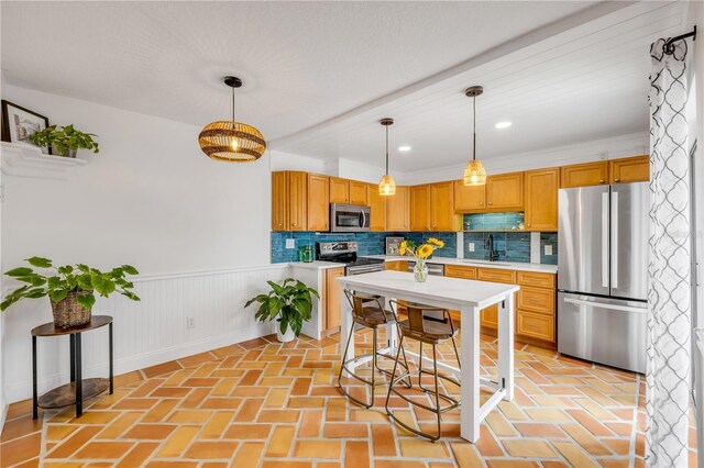 kitchen with appliances with stainless steel finishes, a sink, light countertops, backsplash, and a wainscoted wall