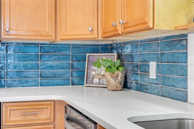 kitchen view of light countertops, stainless steel dishwasher, and backsplash