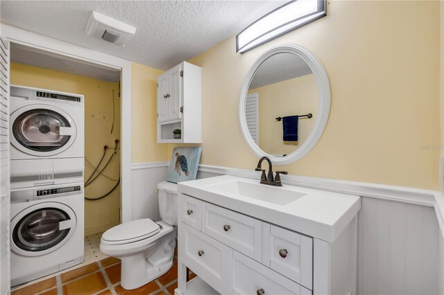 bathroom with estacked washer and dryer, wainscoting, a textured ceiling, toilet, and vanity