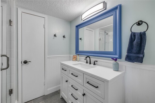bathroom with wainscoting, a textured ceiling, a stall shower, vanity, and a decorative wall