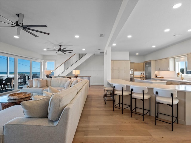 living room featuring light wood-style flooring, recessed lighting, plenty of natural light, ceiling fan, and stairway