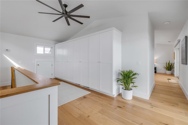 hallway with light wood finished floors, vaulted ceiling, and baseboards