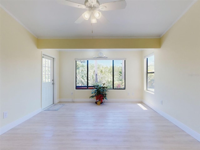 empty room featuring light wood finished floors, plenty of natural light, crown molding, a ceiling fan, and baseboards