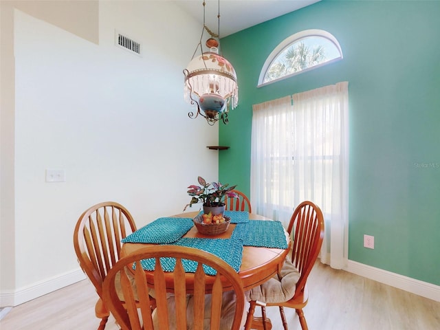 dining space with light wood-type flooring, baseboards, and high vaulted ceiling
