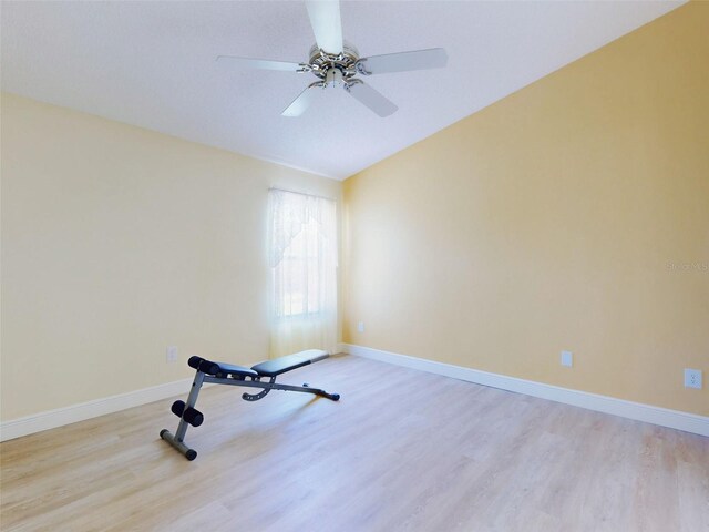 workout area featuring light wood-style floors, a ceiling fan, baseboards, and vaulted ceiling