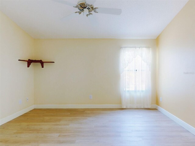 empty room with light wood finished floors, a ceiling fan, and baseboards