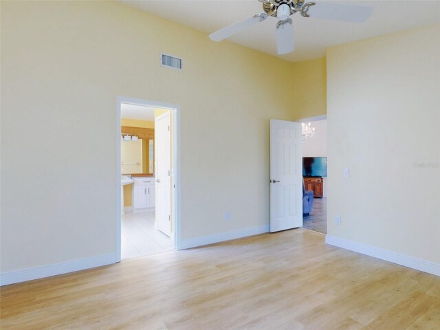 spare room featuring ceiling fan, light wood-style flooring, baseboards, and a towering ceiling
