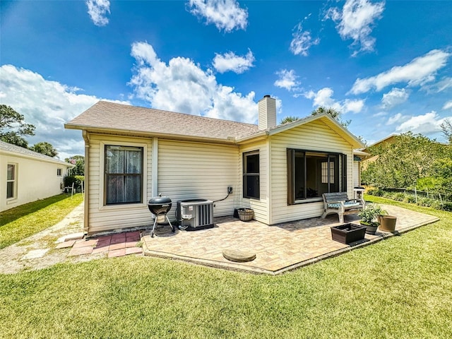 rear view of property with a patio, a yard, a chimney, and central AC