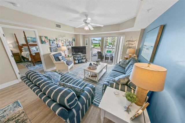 living area with a textured ceiling, wood finished floors, a ceiling fan, and baseboards
