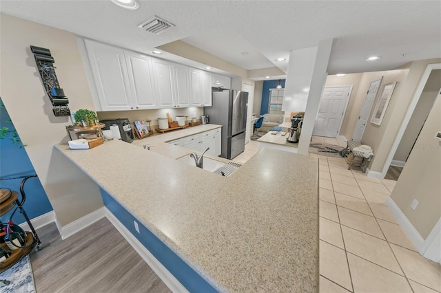 kitchen featuring freestanding refrigerator, a peninsula, light countertops, white cabinets, and baseboards