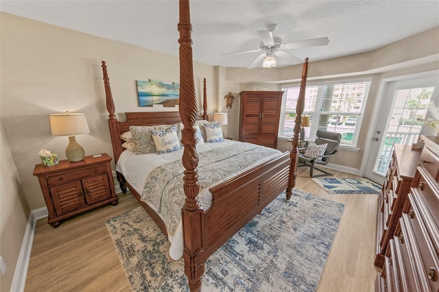 bedroom with access to outside, multiple windows, baseboards, light wood-type flooring, and a textured ceiling
