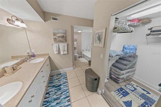 full bath featuring double vanity, tile patterned floors, baseboards, toilet, and a tub