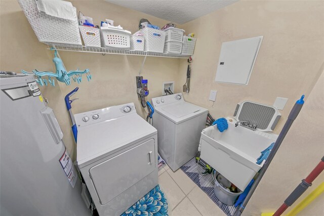 laundry room featuring water heater, washer and clothes dryer, and light tile patterned floors