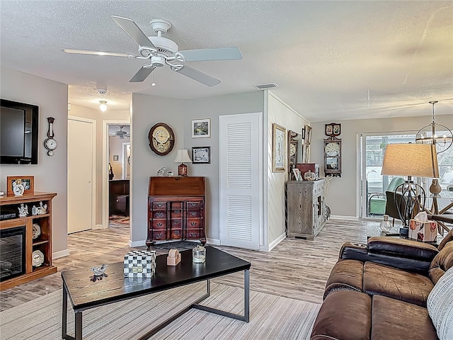 living room with a textured ceiling, ceiling fan, baseboards, and light wood-style flooring