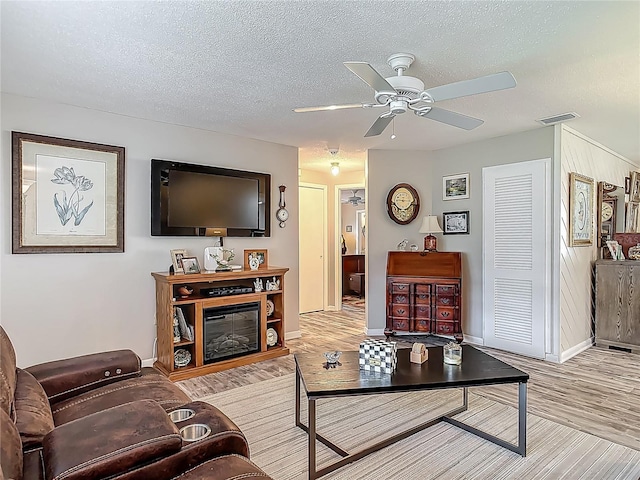 living area featuring a ceiling fan, baseboards, a textured ceiling, and light wood-type flooring
