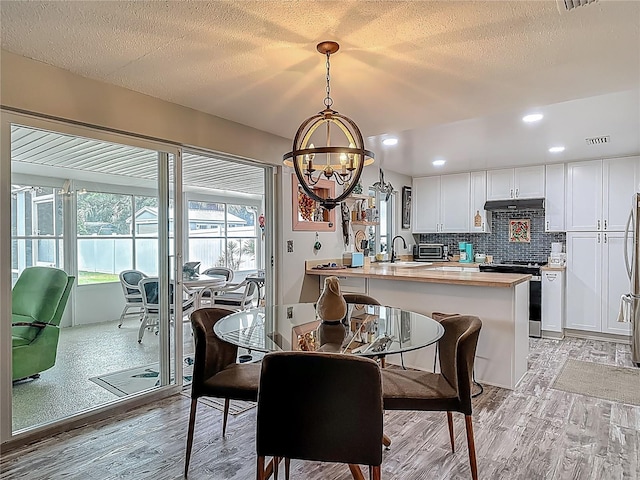 dining room with a chandelier, light wood-style floors, a textured ceiling, and recessed lighting