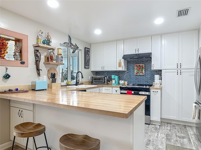 kitchen featuring stainless steel range with electric cooktop, a sink, wooden counters, under cabinet range hood, and a peninsula