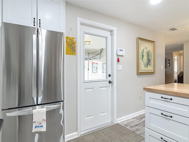 kitchen featuring freestanding refrigerator, butcher block countertops, white cabinets, light wood-style flooring, and baseboards
