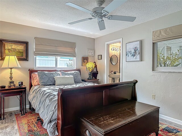 bedroom featuring a textured ceiling, light wood finished floors, baseboards, ceiling fan, and ensuite bath