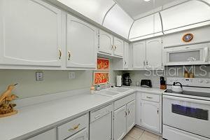 4175 S Atlantic Ave Unit 4050, New Smyrna Beach, FL 32169 - kitchen featuring white appliances, light countertops, light tile patterned floors, a sink, and white cabinets