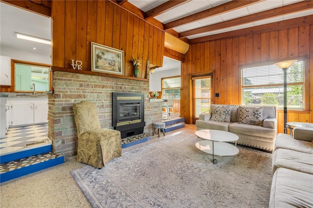 living room with wood walls, a glass covered fireplace, and beam ceiling