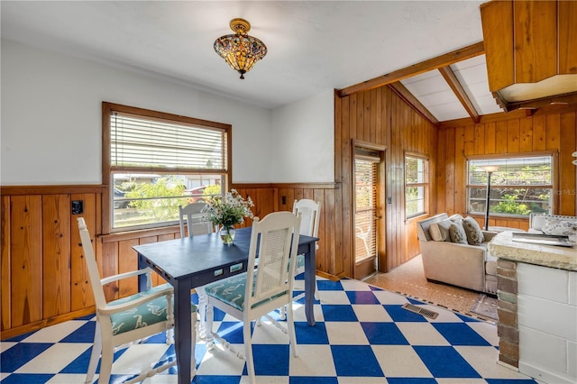 dining room featuring light floors, wood walls, a wainscoted wall, and vaulted ceiling