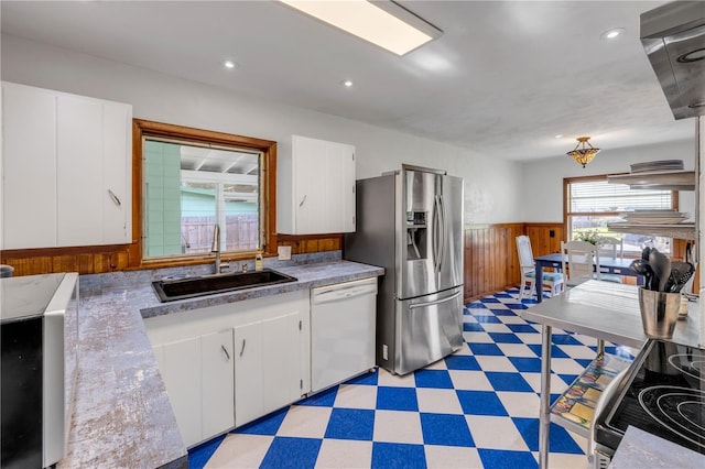 kitchen featuring dishwasher, stainless steel fridge, light floors, a wainscoted wall, and a sink