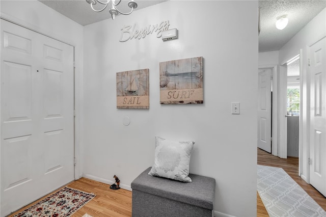 foyer with a textured ceiling, wood finished floors, a chandelier, and baseboards